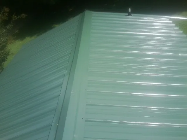 New green metal panels meeting at the ridge of a roof — Flat Roof Repair work by our crew in Edgerton