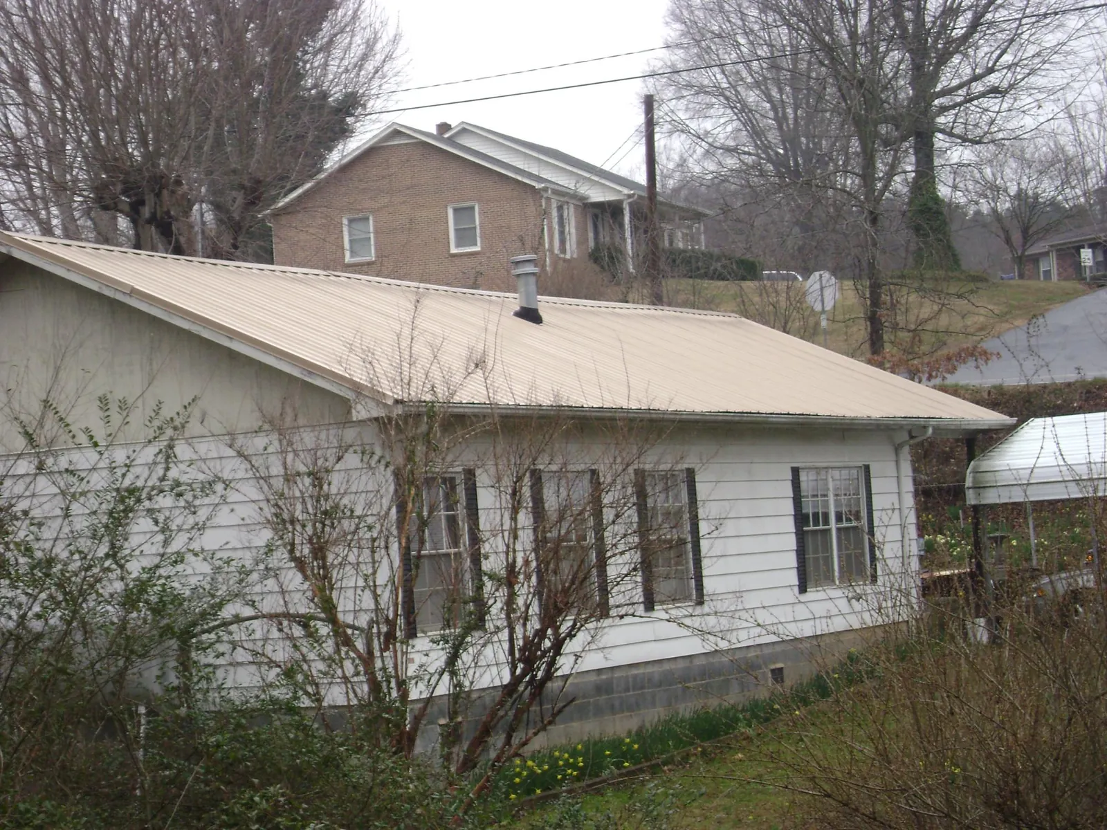 Tan metal roof on a white sided house set into a hillside — Commercial Roofing by Roofing Brothers in Edgerton